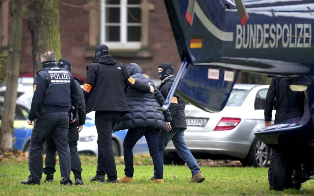 An unnamed suspect, second right, is escorted from a police helicopter by officers in Karlsruhe, Germany, Dec. 7, 2022 (AP Photo/Michael Probst)