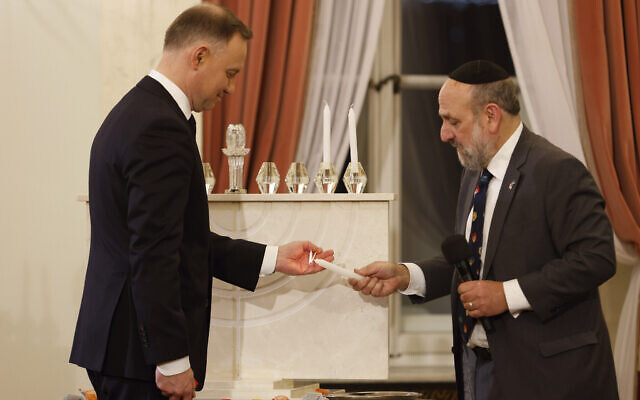 Poland's President Andrzej Duda, left, and the country's chief rabbi, Michael Schudrich, right, light a candle during a Hanukkah ceremony at the presidential palace in Warsaw, Poland, December 19, 2022. (AP Photo/Michal Dyjuk)