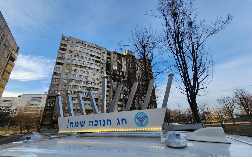 A car with a menorah affixed to the top drives by a bombed-out building in Kharkiv, Ukraine, on the second day of Hanukkah, December 20, 2022 (courtesy Kharkiv Choral Synagogue)
