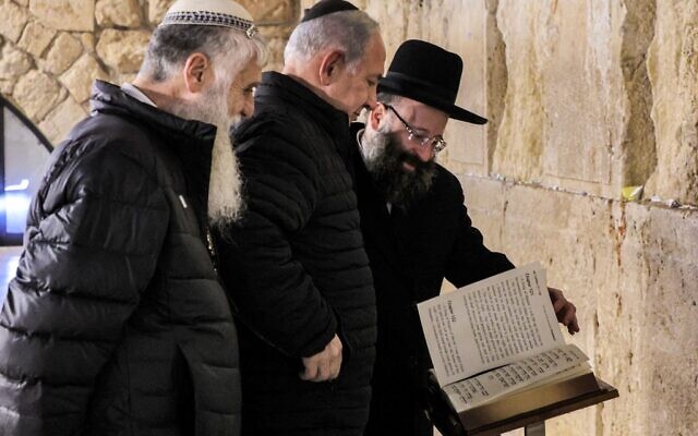 Prime Minister Benjamin Netanyahu (C) reads from the Torah at the Western Wall in Jerusalem accompanied by the Western Wall's Rabbi Shmuel Rabinovitch (R) and the CEO of the Western Wall Heritage Foundation Mordechai Eliav (L), on January 1, 2023. (GIL COHEN-MAGEN / various sources / AFP)