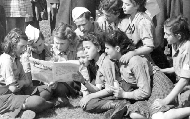 A group of children from the Jaeger Kaserne DP camp in Germany read a Yiddish newspaper in an undated photo. (UN Archives via JTA)
