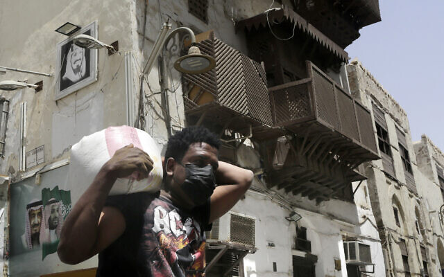 A worker, wearing a face mask as a precaution against the coronavirus, carries a load in Jeddah's historical district, in Jeddah, Saudi Arabia, June 15, 2020. (AP Photo/Amr Nabil)