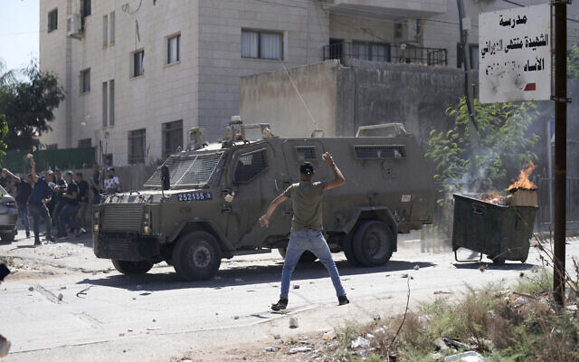 File: Palestinians throw stones at an Israeli military vehicle during a raid in the West Bank city of Jenin, September 28, 2022. (AP Photo/ Majdi Mohammed)