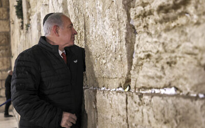 Prime Minister Benjamin Netanyahu places a prayer note between the cracks as he visits the Western Wall in the Old City of Jerusalem, January 1, 2023. (Gil Cohen-Magen/Pool via AP)