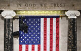 'In God We Trust' is engraved in stone above a U. flag in the House of Representatives chamber at the Capitol in Washington on Tuesday, March 1, 2022.(Sarahbeth Maney/The New York Times via AP, Pool)