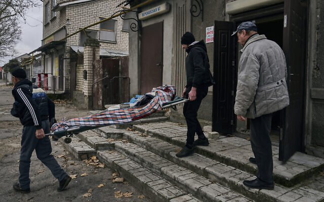 Local residents carry the body of a 20-year-old man killed in Russian shelling in Kherson, Ukraine, Thursday, January 5, 2023. (AP Photo/LIBKOS)