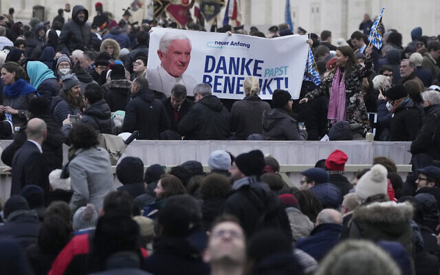 People hold a banner as they gather in St. Peter's Square at the Vatican for the funeral mass for late Pope Emeritus Benedict XVI, Thursday, Jan. 5, 2023. Benedict died at 95 on Dec. 31 in the monastery on the Vatican grounds where he had spent nearly all of his decade in retirement, his days mainly devoted to prayer and reflection. (AP Photo/Alessandra Tarantino)