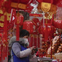 A vendor wearing a face mask checks her smartphone at her store selling Chinese Lunar New Year decorations in Beijing, January 7, 2023. (AP/Andy Wong)