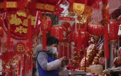 A vendor wearing a face mask checks her smartphone at her store selling Chinese Lunar New Year decorations in Beijing, January 7, 2023. (AP/Andy Wong)