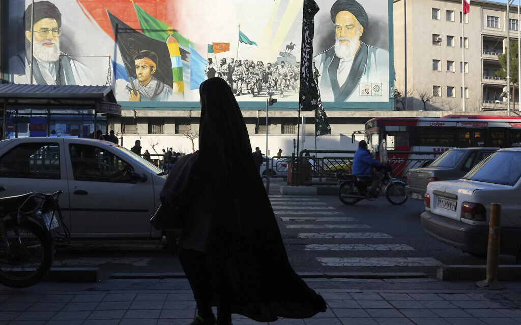 A woman, wearing the chador, a head-to-toe garment, walks on a sidewalk in front of a mural showing the late Iranian revolutionary founder Ayatollah Khomeini, right, Supreme Leader Ayatollah Ali Khamenei, left, and Basij paramilitary force, at Enqelab-e-Eslami (Islamic Revolution) street, in downtown Tehran, Iran, Jan. 7, 2023. (AP Photo/Vahid Salemi)