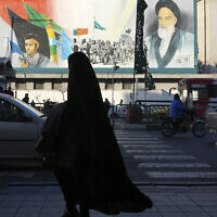 A woman, wearing the chador, a head-to-toe garment, walks on a sidewalk in front of a mural showing the late Iranian revolutionary founder Ayatollah Khomeini, right, Supreme Leader Ayatollah Ali Khamenei, left, and Basij paramilitary force, at Enqelab-e-Eslami (Islamic Revolution) street, in downtown Tehran, Iran, Jan. 7, 2023. (AP Photo/Vahid Salemi)