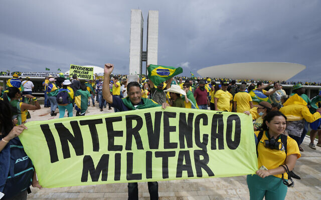 Protesters, supporters of Brazil's former President Jair Bolsonaro, hold a banner that reads in Portuguese " Military Intervention" as they storm the the National Congress building in Brasilia, Brazil, Sunday, Jan. 8, 2023. (AP/Eraldo Peres)