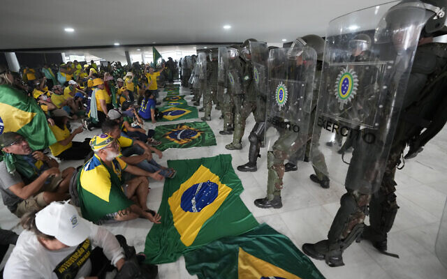 Protesters, supporters of Brazil's former President Jair Bolsonaro, sit in front of police after inside Planalto Palace after storming it, in Brasilia, Brazil, Sunday, Jan. 8, 2023. (AP/Eraldo Peres)