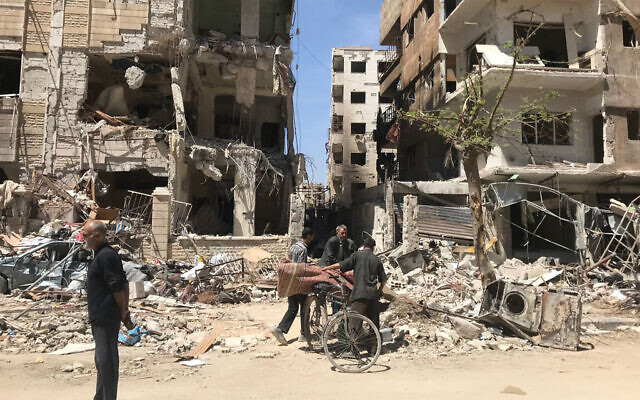 People stand in front of damaged buildings, in the town of Douma, the site of a suspected chemical weapons attack, near Damascus, Syria, Monday, April 16, 2018. (AP Photo/Hassan Ammar, File)