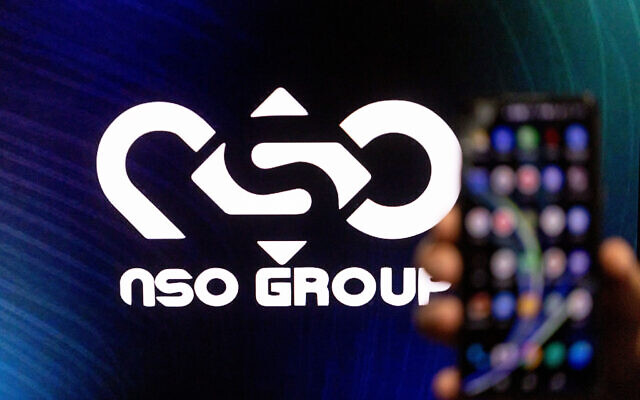 Illustrative. A man holds his phone with NSO GROUP logo on a computer screen in the background, in Jerusalem, on February 7, 2022. (Yonatan Sindel/Flash90)