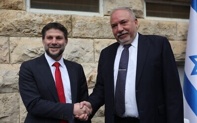 New Finance Minister Bezalel Smotrich, left, shakes hands with outgoing minister Avigdor Liberman at a handover ceremony at the Finance Ministry in Jerusalem, January 1, 2023. (Yonatan Sindel/FLASH90)