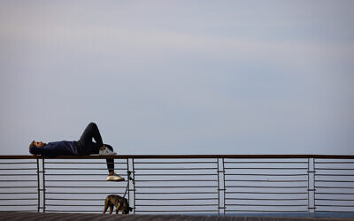 A person lies on a railing at a Tel Aviv promenade in the northern part of the city, January 11, 2023. (Olivier Fitoussi/Flash90)