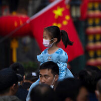 A girl wearing a face mask rides on a man's shoulders as they walk along a tourist shopping street in Beijing, October 7, 2022. (AP Photo/Mark Schiefelbein, File)