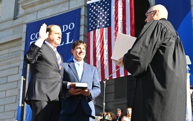 Brian Boatright, the chief justice of the Colorado Supreme Court, at right, swears in Gov. Jared Polis, on the left, while Polis's husband, Marlon Reis, holds a Hebrew bible, in Denver, Jan. 10, 2023. (Gov. Jared Polis Facebook page via JTA)