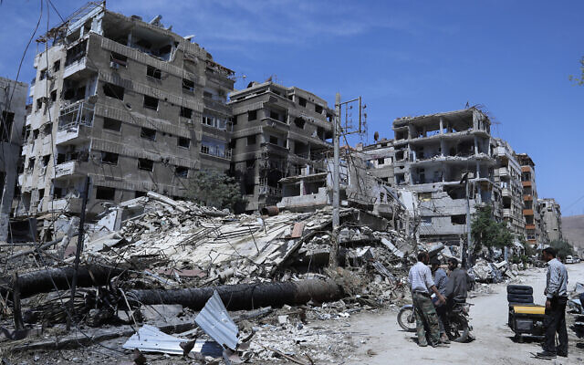 People stand in front of damaged buildings in the town of Douma, the site of a suspected chemical weapon attack, near Damascus, Syria, on April 16, 2018. (Hassan Ammar/AP)