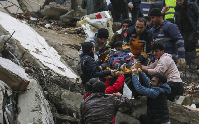 People and emergency teams rescue a person on a stretcher from a collapsed building in Adana, Turkey, Feb. 6, 2023. (IHA agency via AP)