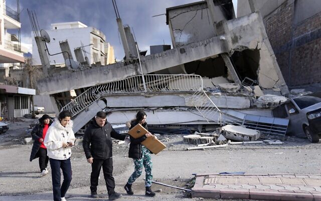 People pass a destroyed building, in Iskenderun town, southern Turkey, Tuesday, February 7, 2023. (AP Photo/Hussein Malla)