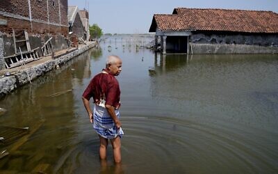File: Sukarman walks on a flooded pathway outside his house in Timbulsloko, Central Java, Indonesia, July 30, 2022. (AP/Dita Alangkara)
