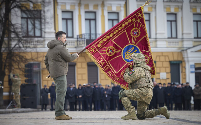 Ukrainian President Volodymyr Zelensky, left, holds the flag of a military unit as an officer kisses it, during commemorative event on the occasion of the Russia Ukraine war one year anniversary in Kyiv, Ukraine, February 24, 2023. (Ukrainian Presidential Press Office via AP)