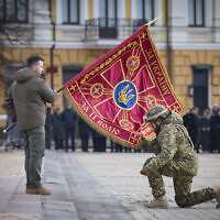 Ukrainian President Volodymyr Zelensky, left, holds the flag of a military unit as an officer kisses it, during a commemorative event on the occasion of the one year anniversary of the Russia Ukraine war in Kyiv, Ukraine, February 24, 2023. (Ukrainian Presidential Press Office via AP)