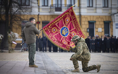 Ukrainian President Volodymyr Zelensky, left, holds the flag of a military unit as an officer kisses it, during a commemorative event on the occasion of the one year anniversary of the Russia Ukraine war in Kyiv, Ukraine, February 24, 2023. (Ukrainian Presidential Press Office via AP)