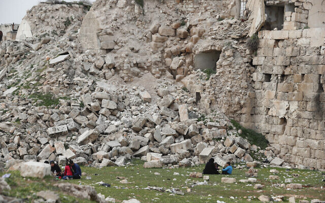 People sit by a building destroyed in recent earthquake in Aleppo, Syria, February 27, 2023. (Omar Sanadiki/AP)