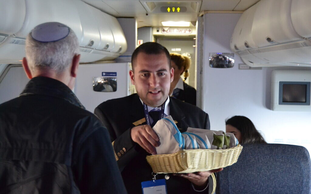 Idan Fishslevich, a 22-year-old with high functioning ASD who was made a flight attendant for one day, is seen serving passengers onboard flight LY383 from Tel Aviv Rome, February 20, 2023. (Tobias Siegal/The Times of Israel)