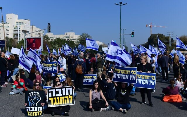 Israelis hold signs and wave the Israeli flag as they walk in the streets of Tel Aviv, protesting the government's planned judicial overhaul, February 20, 2023. (Tomer Neuberg/FLASH90)