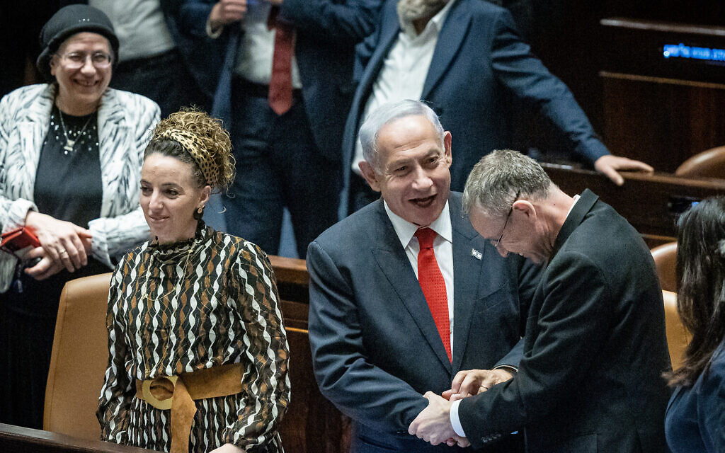 Prime Minister Benjamin Netanyahu shakes hands with Justice Minister Yariv Levin, as other coalition members look on, after a vote on the government's judicial overhaul plans in the Knesset early on February 21, 2023. (Yonatan Sindel/Flash90)