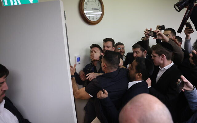 Security guards grab and throw out an anti-government protester who interrupted Shas party leader Aryeh Deri's speech during a faction meeting at the Knesset in Jerusalem, February 13, 2023. (Yonatan Sindel/Flash90)