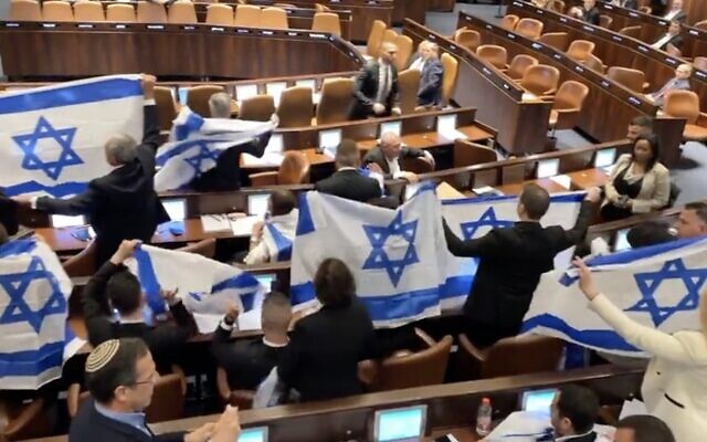 Opposition MKs raise Israeli flags to protest the government's judicial overhaul plans, during a Knesset plenum session, February 20, 2023. (Twitter video screenshot; used in accordance with Clause 27a of the Copyright Law)