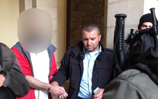 A US tourist, left, is led away by police on suspicion that he vandalized a statue in the Church of the Flagellation in the Old City of Jerusalem, February 2, 2023. (Israel Police)