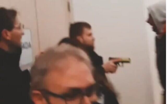 In a screenshot from video on social media, an armed guard holds a gun across from pro-BDS activists who interrupted a lecture by Israel's ambassador to Spain, Rodica Radian-Gordon, at Complutense University of Madrid, February 8, 2023. (Twitter screenshot; used in accordance with Clause 27a of the Copyright Law)