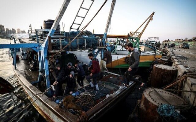Palestinian fisherman Jihad al-Hissi and his sons work on their boat at the seaport in Gaza City on January 10, 2023. (MAHMUD HAMS/AFP)