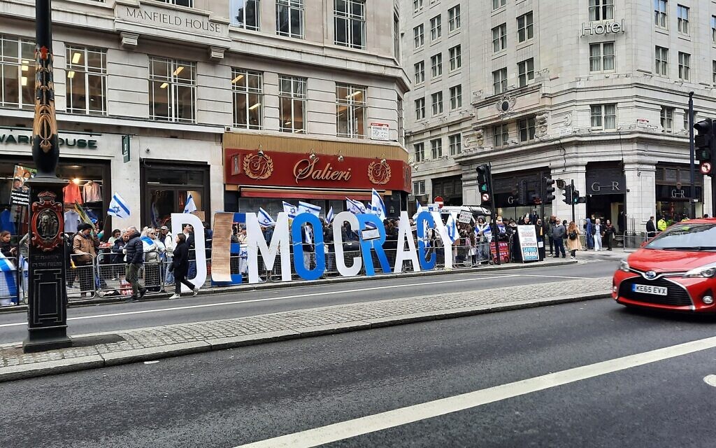A sign reading 'Democracy' adorned with Israel's Declaration of Independence at a protest outside the Savoy Hotel in London where Prime Minister Benjamin Netanyahu was staying on March 24, 2023. (Amy Spiro/Times of Israel)