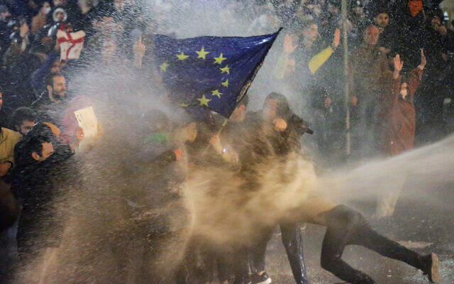 Protesters carrying a European Union flag are sprayed by a water cannon during clashes with riot police near the Georgian parliament in Tbilisi on March 7, 2023. (AFP)
