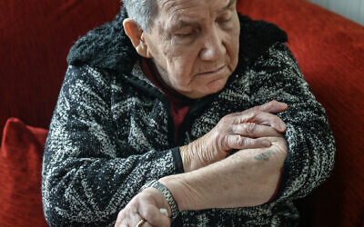 Holocaust survivor Naki Bega looks at her Auschwitz-Birkenau serial-number digits tattooed on her skin, as she poses at her daughter's home in Athens, Greece, on March 14, 2023. (Louisa GOULIAMAKI/AFP)