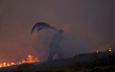 A volunteer is engulfed in smoke while using a tree branch to try to stop a wildfire in Gouveia, in the Serra da Estrela mountain range in Portugal, August 18, 2022. Authorities in Portugal said they had brought under control a wildfire that for almost two weeks raced through pine forests in the Serra da Estrela national park, but later in the day a new fire started and threatened Gouveia. (AP Photo/Joao Henriques)