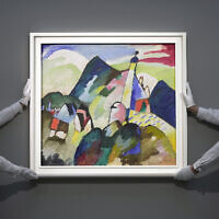 Members of staff hold the painting 'Murnau with Church II' by Russian artist Wassily Kandinsky in 1910 is on display during a media preview of Sotheby's auction, in London, February 22, 2023.  (AP Photo/Kin Cheung)
