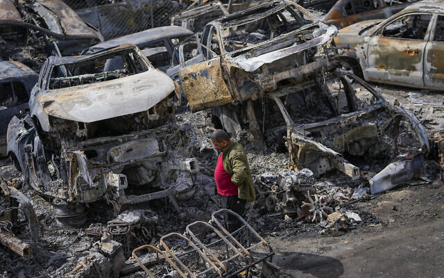 A Palestinian man walks between scorched cars in a scrapyard, in the town of Hawara, near the West Bank city of Nablus, Feb. 27, 2023 (AP Photo/Ohad Zwigenberg)