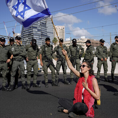 A demonstrator waves the Israeli flag seated on a highway while flanked by border police during a protest against plans by Prime Minister Benjamin Netanyahu's government to overhaul the judicial system, in Tel Aviv, Israel, March 9, 2023. (AP Photo/Ariel Schalit)