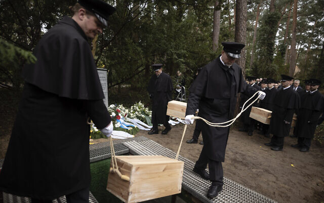 Caskets containing bones found on the grounds of the Freie Universitat, Free University are lowered into the ground for burial, at the Waldfriedhof in Berlin, Germany, Thursday, March 23, 2023. (AP Photo/Markus Schreiber)
