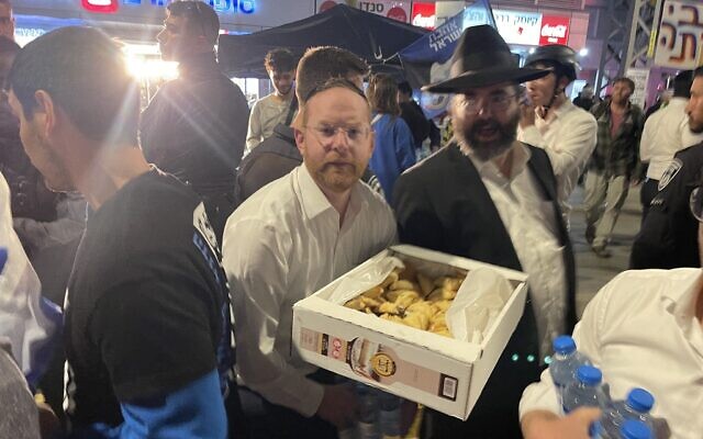 An ultra-Orthodox man hands out Hamentaschen to protesters in Bnei Brak on March 23, 2023. (Carrie Keller-Lynn/Times of Israel)