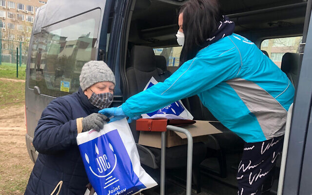 An employee of the American Jewish Joint Distribution Committee, right, hands out an aid package to a Jewish woman in Kharkiv, Ukraine during the coronavirus pandemic in March 2020. (Courtesy of JDC)