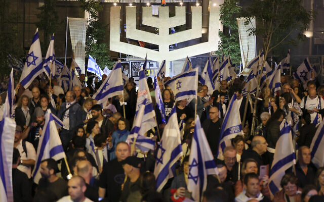 Demonstrators hold flags and raise a menorah during a rally in Tel Aviv to protest the Israeli government's judicial overhaul bill, as the country begins celebrations for its 75th anniversary, on April 25, 3023. (Photo by JACK GUEZ / AFP)